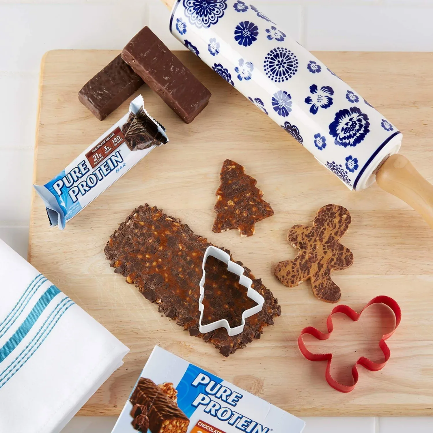 A Pure Protein bar flattened with a rolling pin and cut with tree and gingerbread-man cookie cutters on a wooden board.